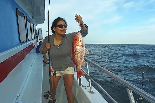 Smilling woman holding up a fish on a fishing party boat