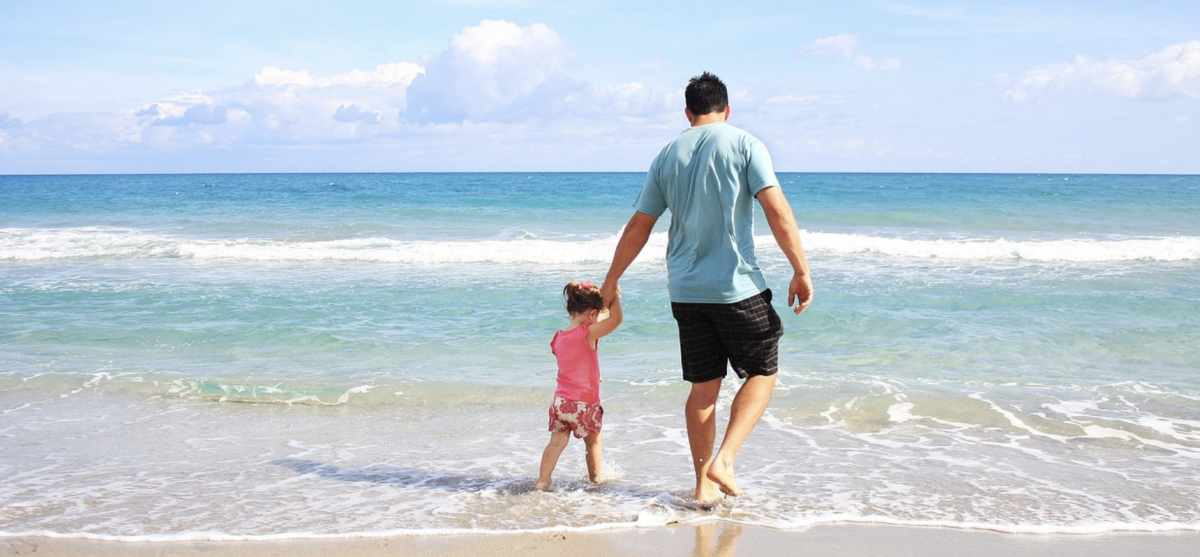 A father holds his young daughters hand as they walk into the ocean