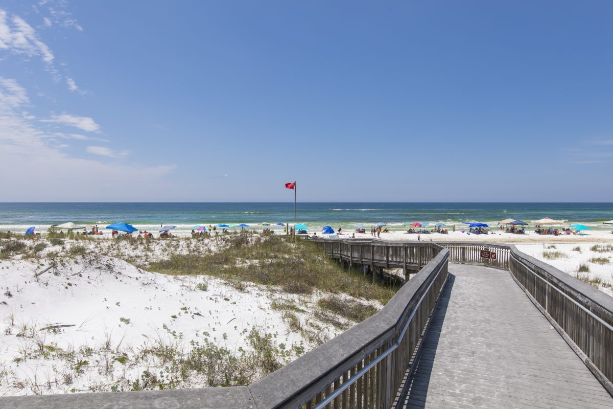 A wooden staircase leads to a beach shoreline with an abundance of lounge chairs, tents, & umbrellas set up